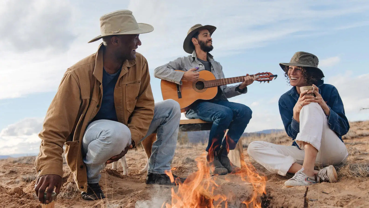 Four friends by a campfire wearing Tilley hats in a cozy outdoor setting.