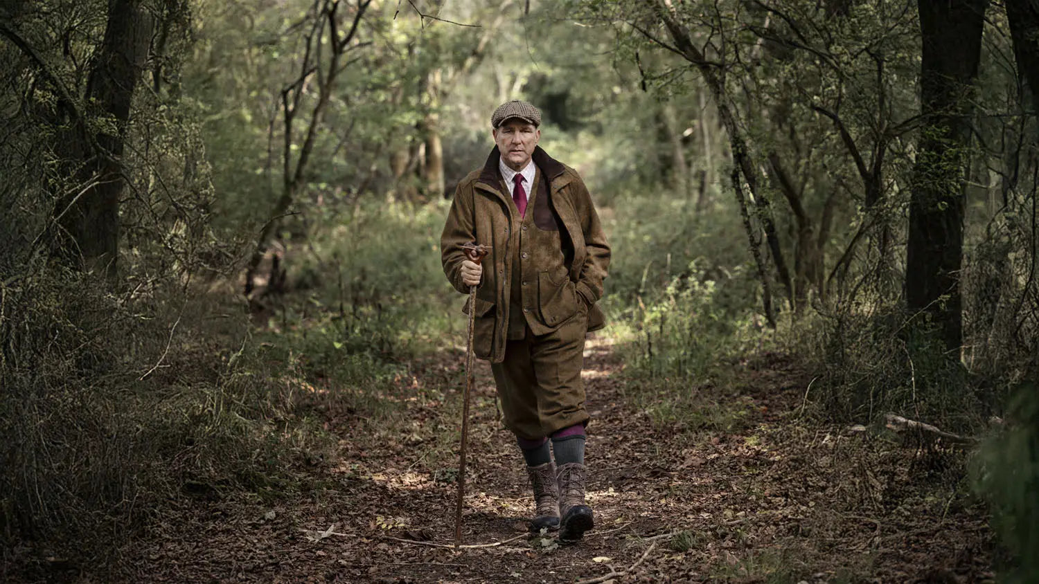 Man in tweed suit with walking stick showcasing modern sophistication from the Gentlemen Collection.