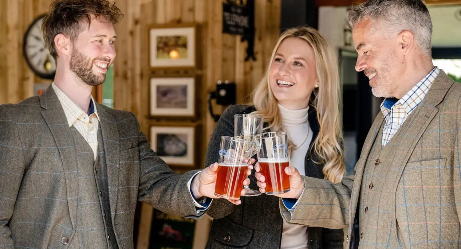 Three friends toasting with beers while wearing stylish mens blazers at a gathering.