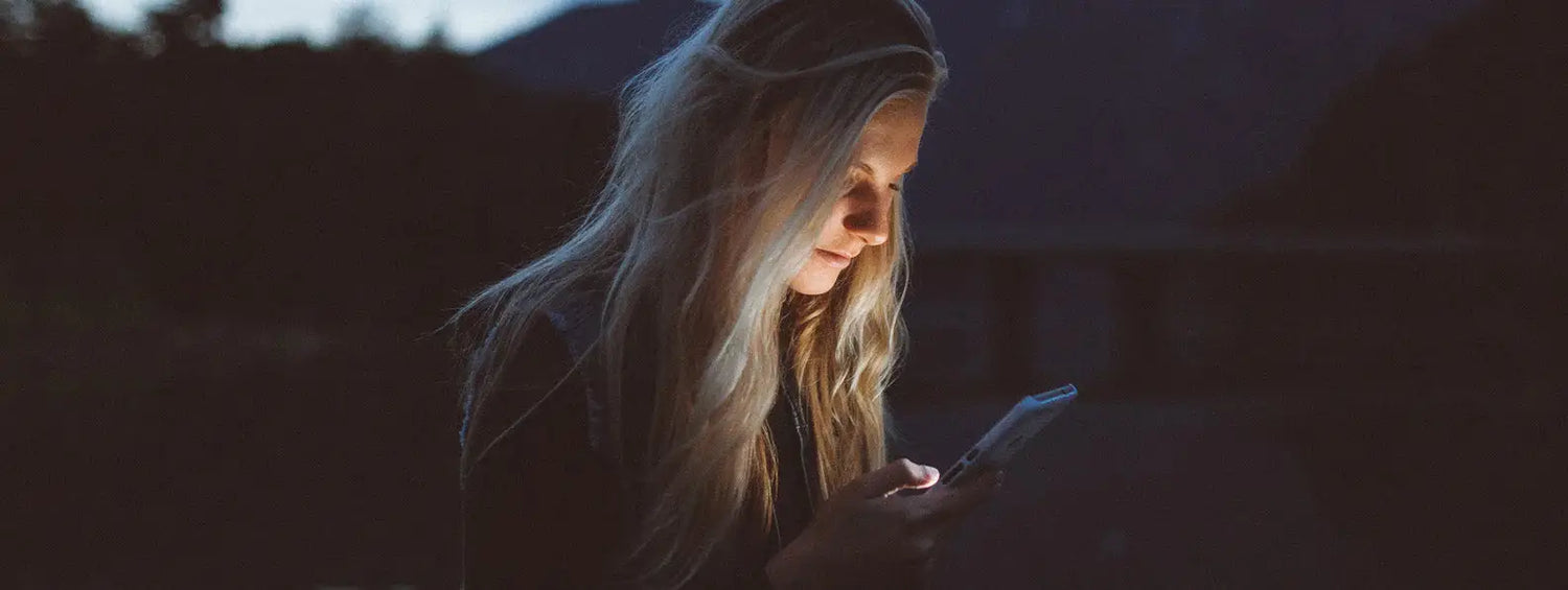 Person with long blonde hair in darkness holding smartphone, checking exclusive special offers.