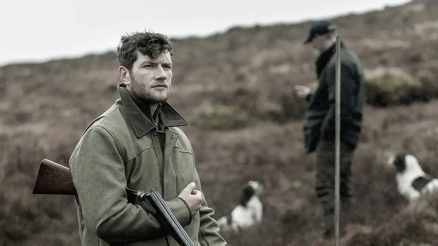 Man in a green jacket with a rifle showcasing quality country clothing in rural setting.