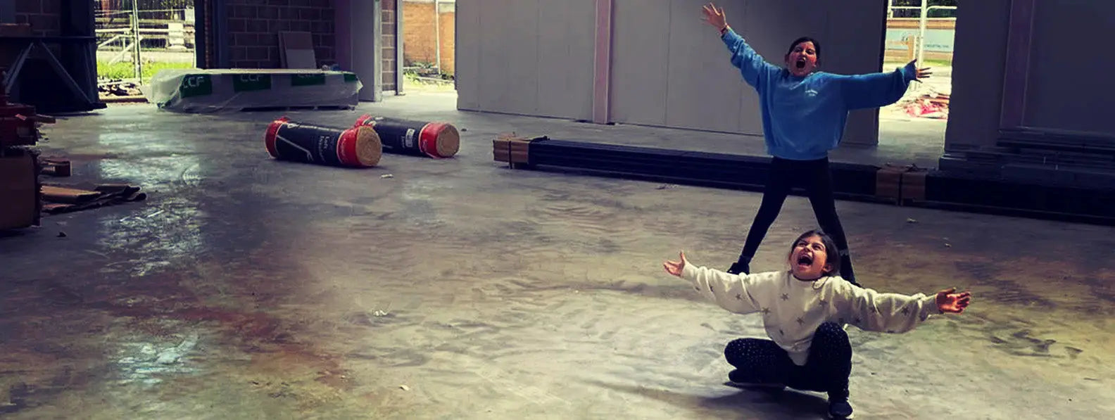 Two friends showing off stylish outdoor clothing on a wet concrete floor in the New Forest.