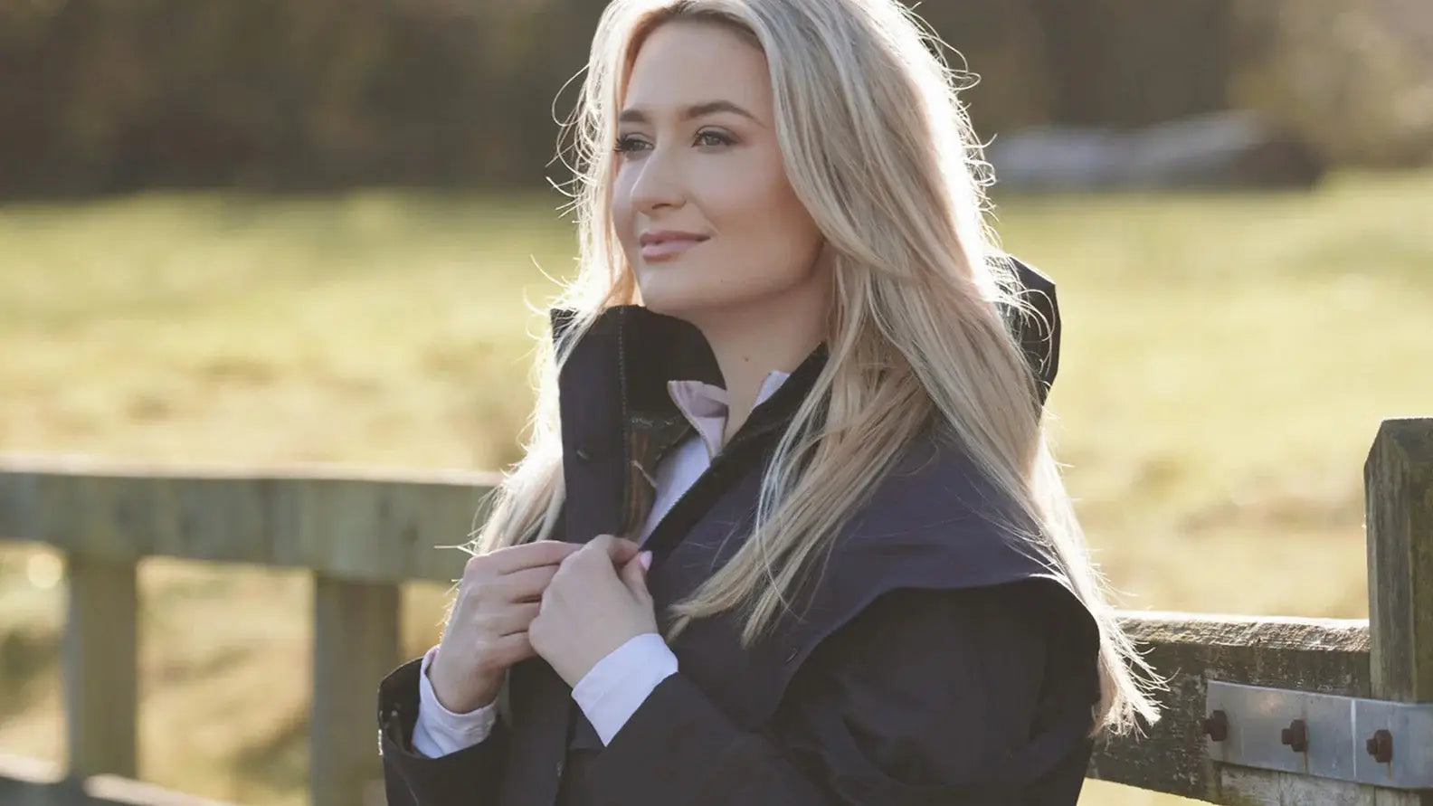 Blonde woman in a black coat outdoors showcasing the stylish Victoria Cape for dog walkers.