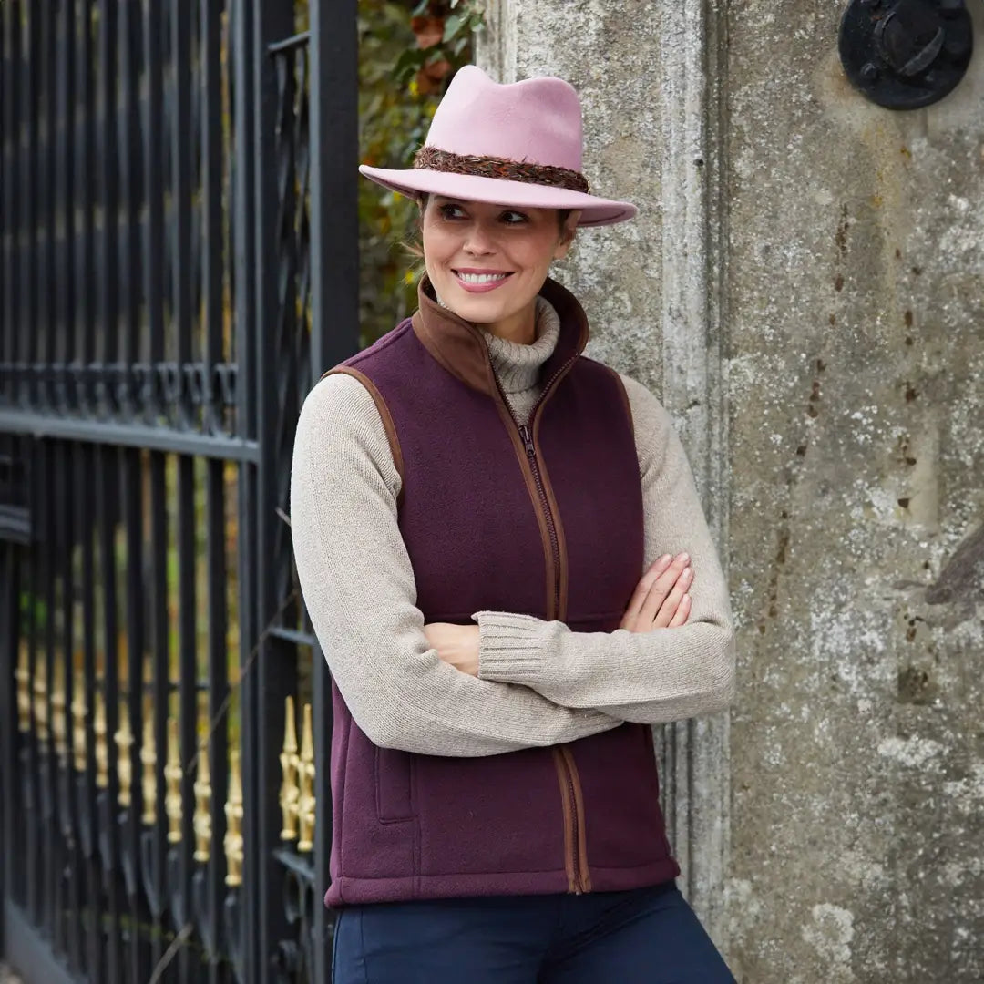 Woman smiling in a pink hat and purple vest, showcasing Alan Paine Aylsham Ladies Fleece Gilet