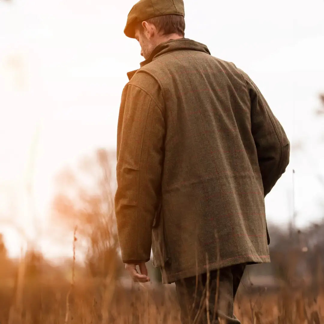 Man in a flat cap and overcoat strolling through a field in style with a tweed flat cap