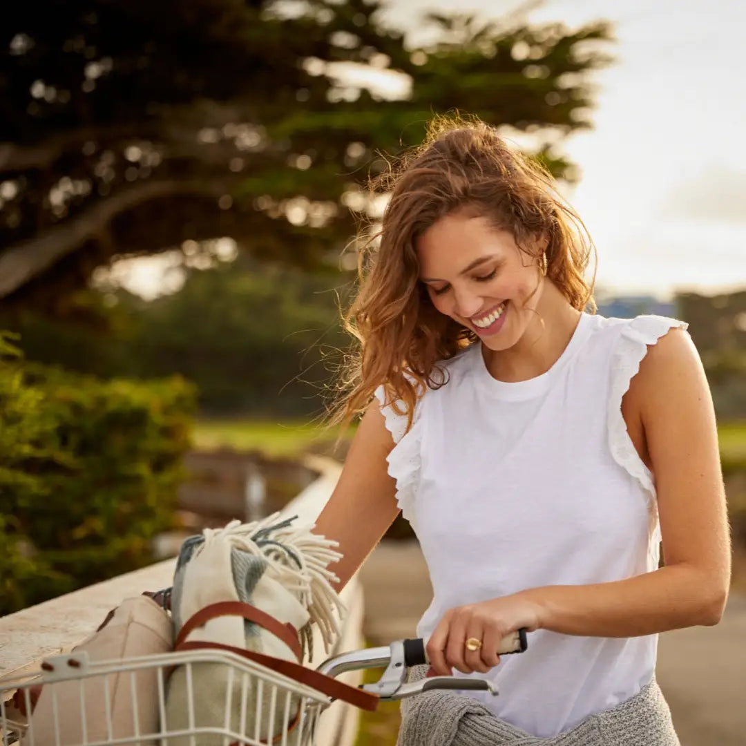 Smiling woman in white sleeveless top biking, perfect for country clothing adventures