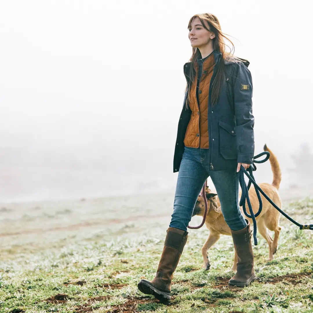 Woman in country clothing walking a dog in misty field with tall waterproof boots