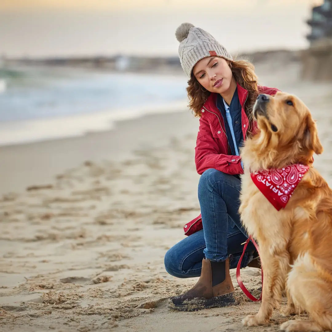 Golden Retriever in a red bandana beside a person in waterproof country boots on the beach