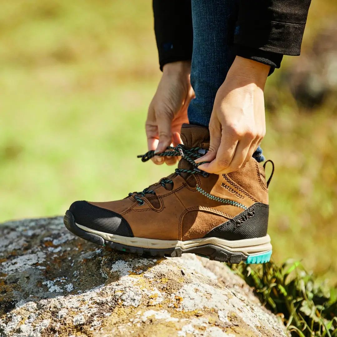 Ariat Womens Skyline Mid Waterproof Boots being laced on a rocky surface