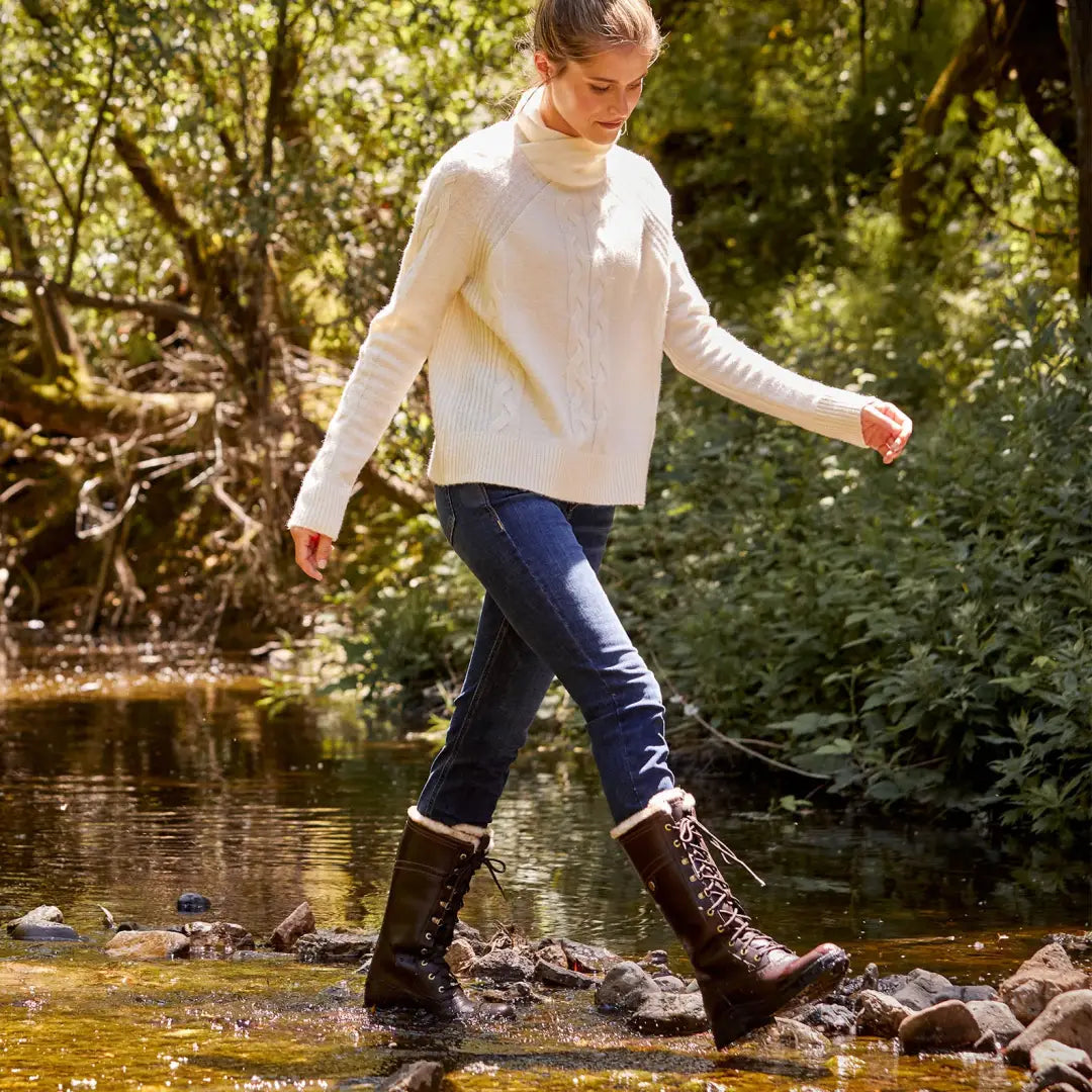 Person in a white sweater and Ariat Wythburn II boots crossing a stream in the outdoors