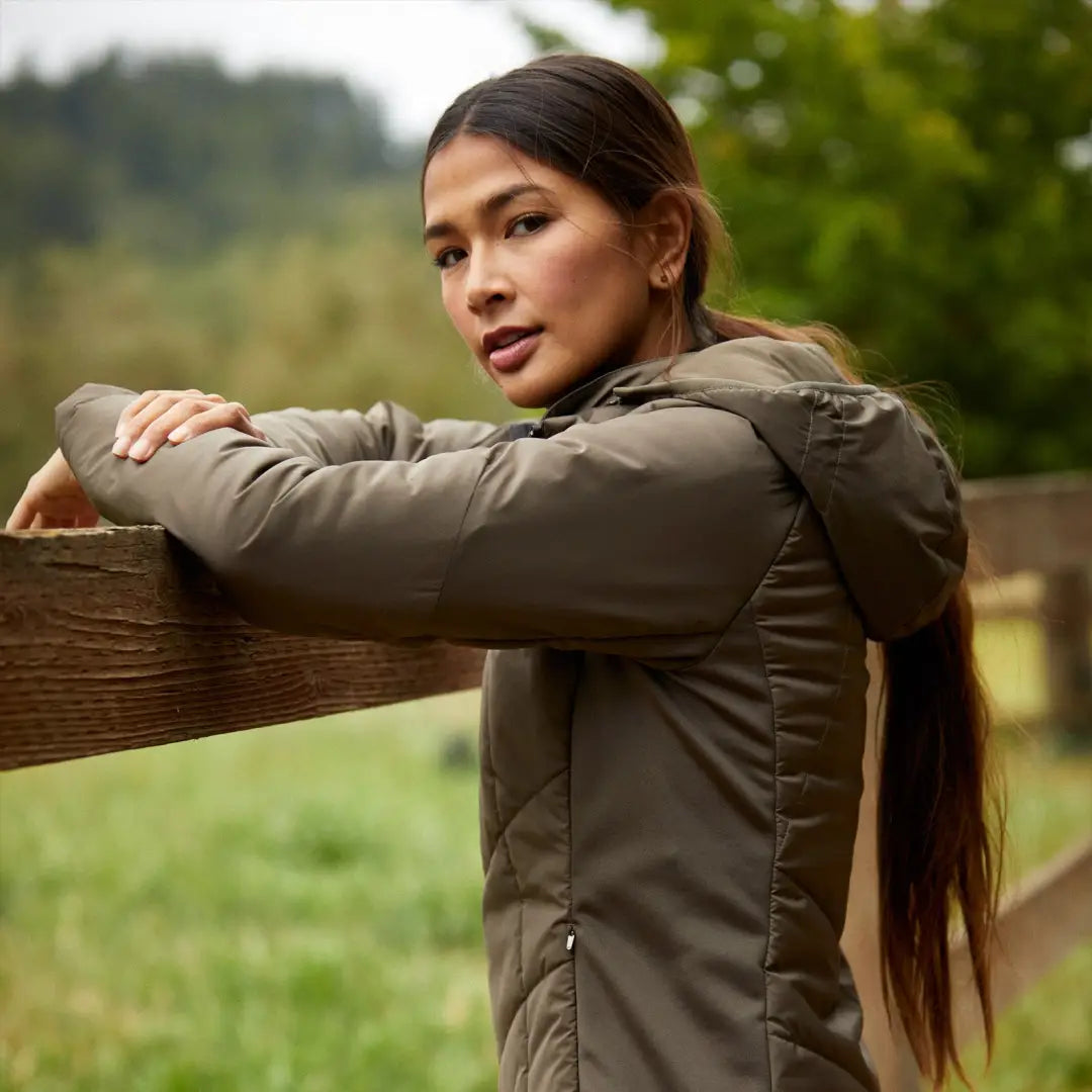 Woman in an olive green Zonal Insulated Jacket leaning on a wooden fence