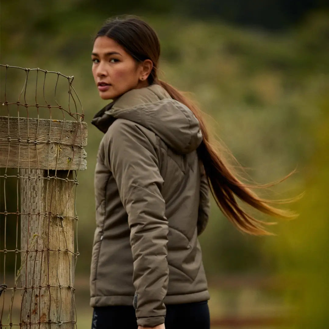 Woman with long dark hair in a brown Zonal Insulated Jacket, looking back stylishly