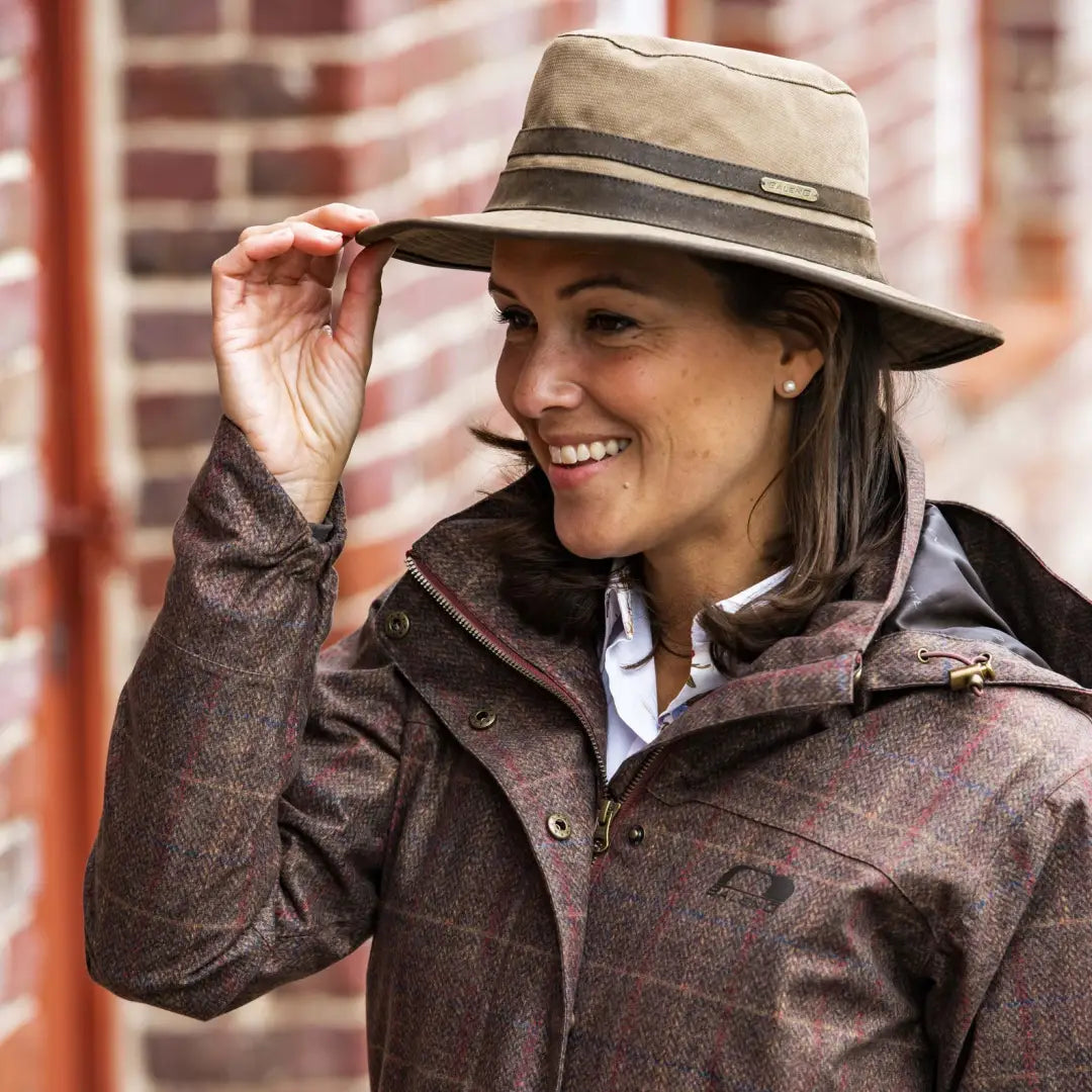 Smiling woman in a beige fedora sporting the Baleno Edith Waterproof Hat and brown jacket