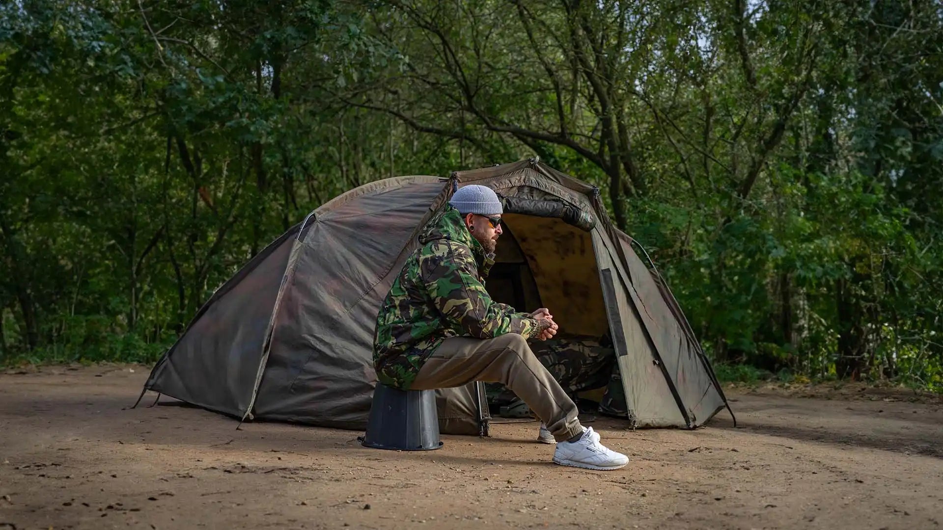 Camouflage tent with seated man.