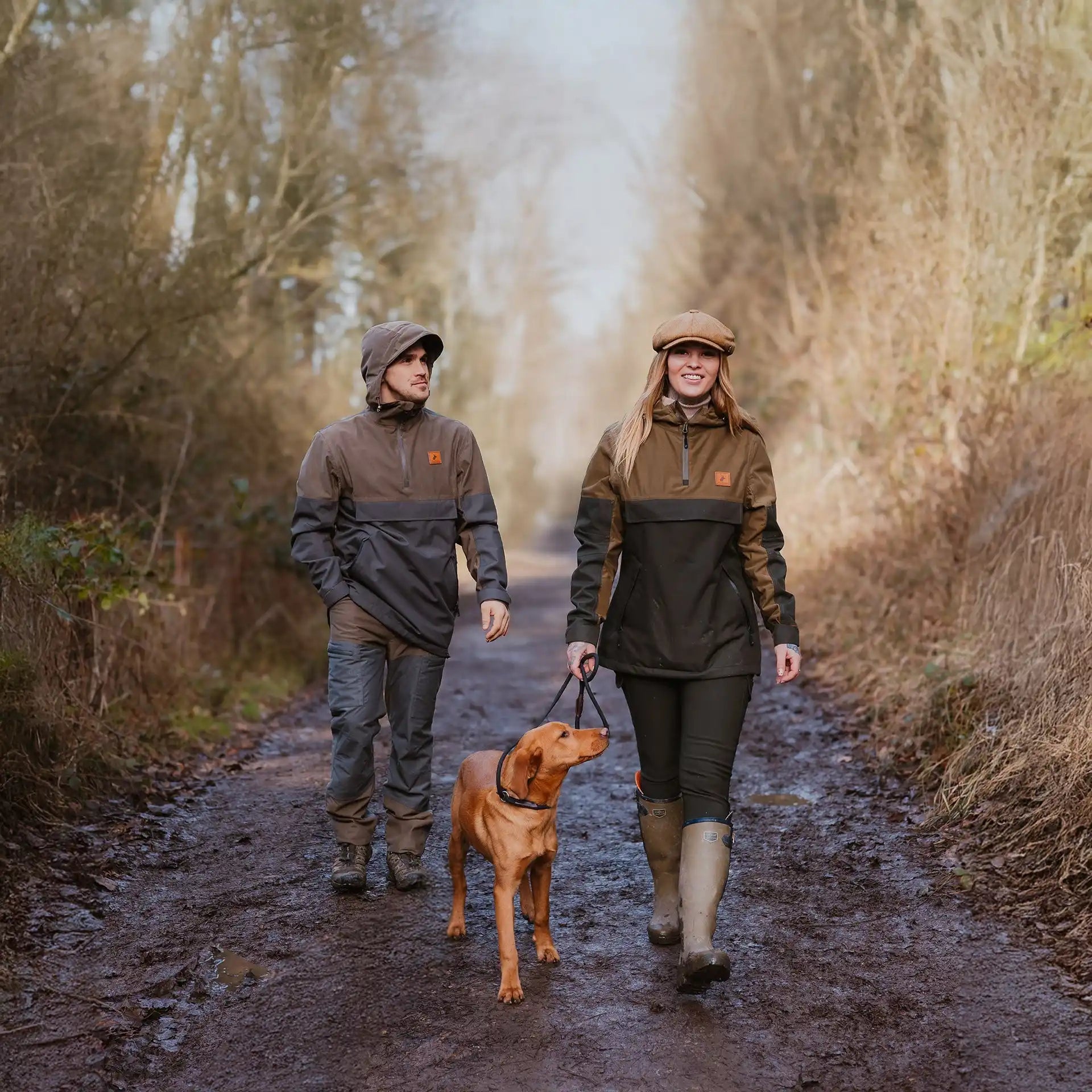 Couple walking a dog in matching outdoor wear.