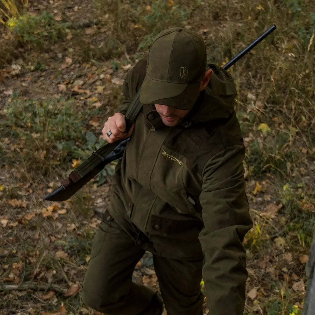 Hunter in dark green gear with rifle showcasing Deerhunter Eagle Cap for hunting essentials