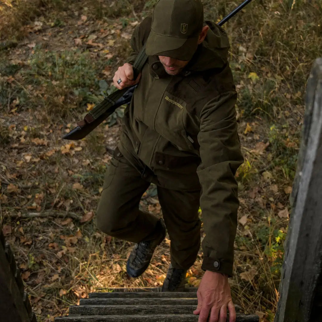 Person in dark green hunting gear climbing a ladder wearing an Eagle Jacket for active hunts