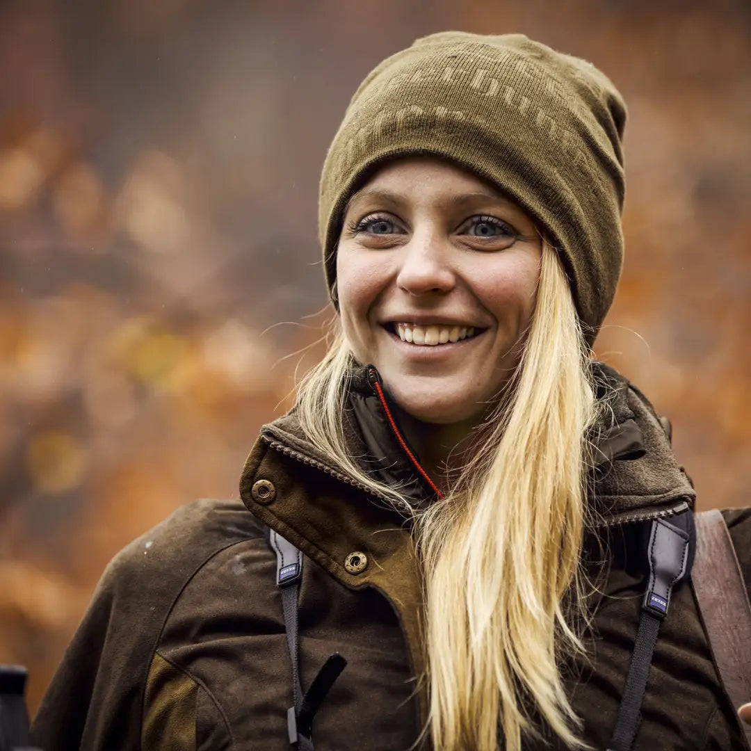 Smiling person in a green beanie and brown jacket wearing a Deerhunter Embossed Logo Hat