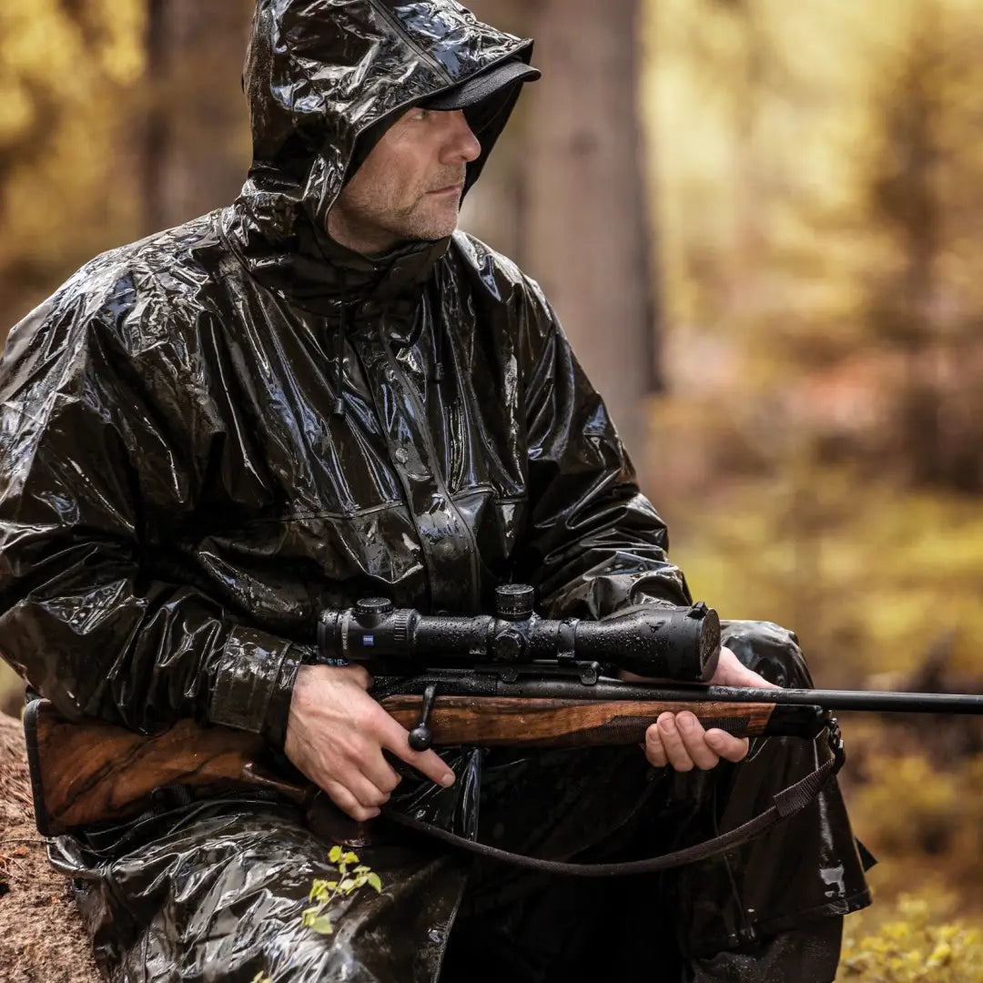 Hunter in Deerhunter Hurricane long raincoat, holding rifle with scope in rain