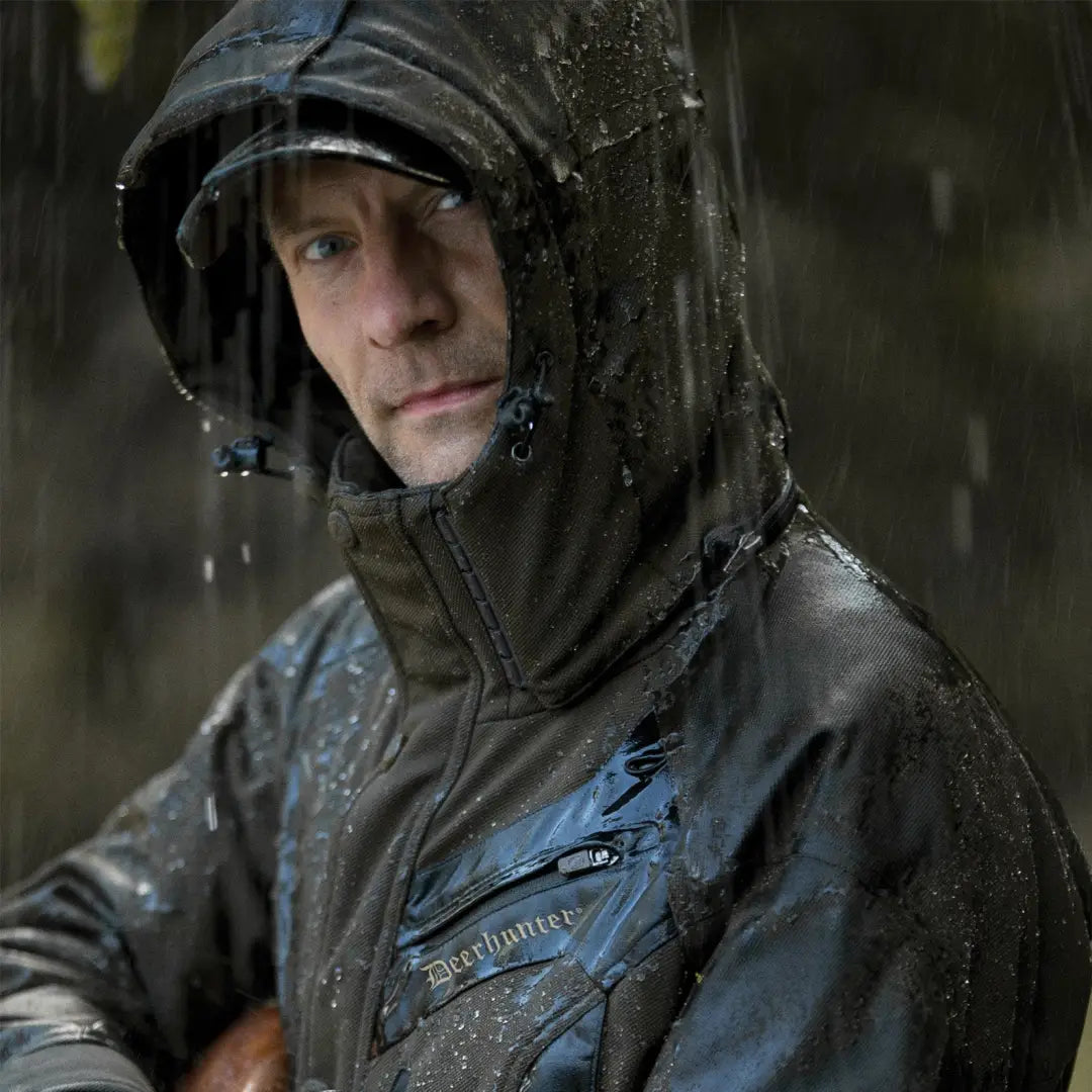 Person in a dark hooded raincoat wearing Deerhunter Muflon Long Jacket in the rain