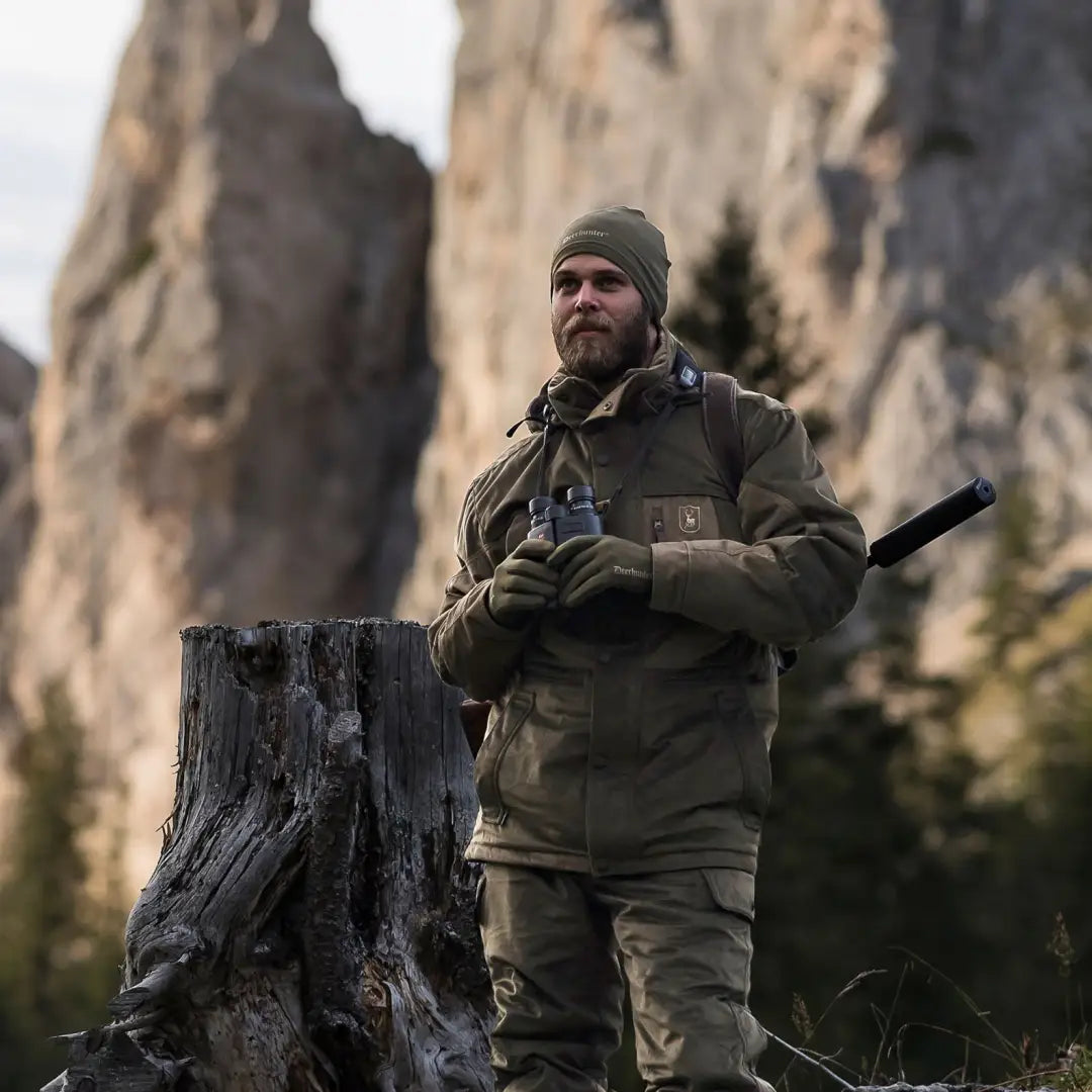 Man in military-style gear by a tree stump wearing Rusky Silent Gloves in the mountains