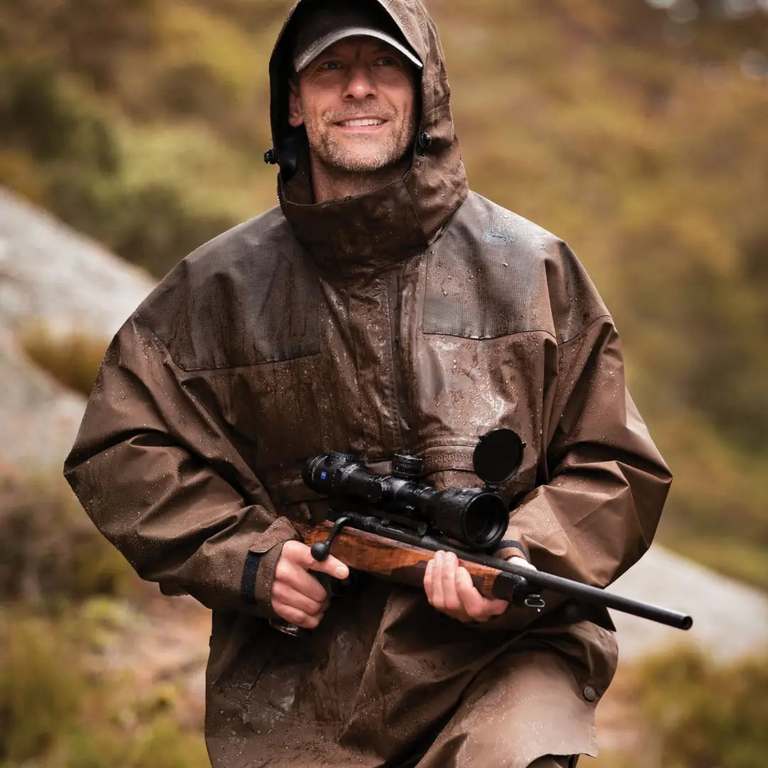 Smiling hunter in Deerhunter Track Rain Anorak holding a rifle with scope