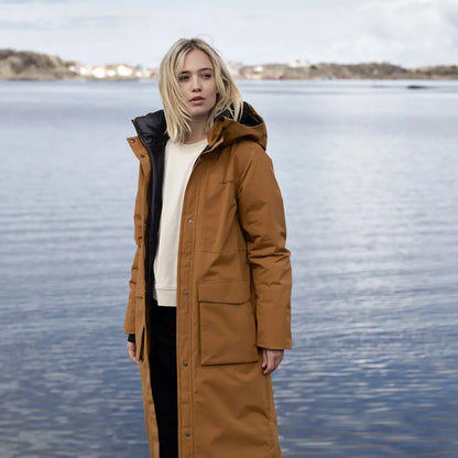 Woman wearing Didriksons Leya Long Womens Parka 2 by the water in a stylish brown coat