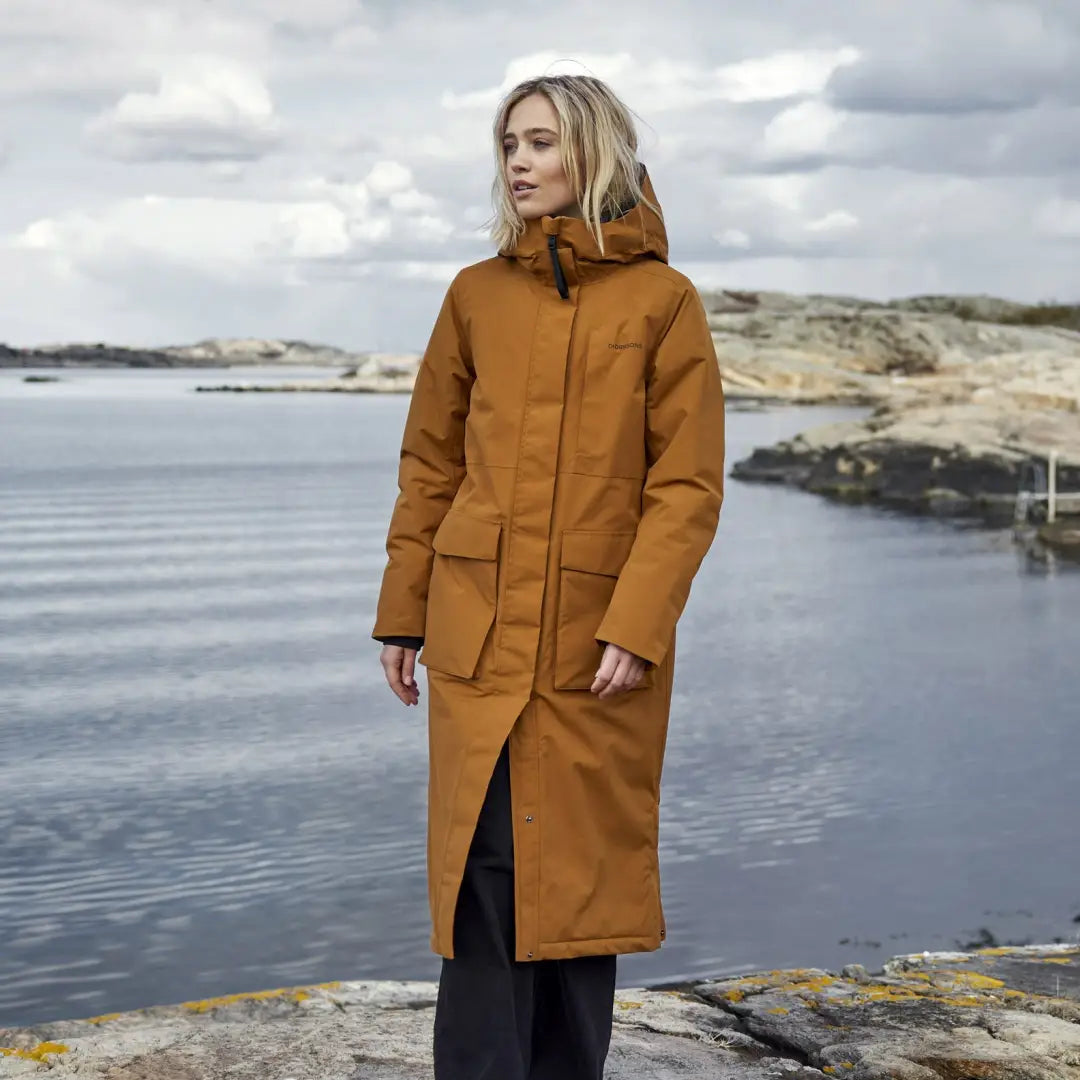 Woman in a long orange winter coat by water, styling the Leya Long Womens Parka 2