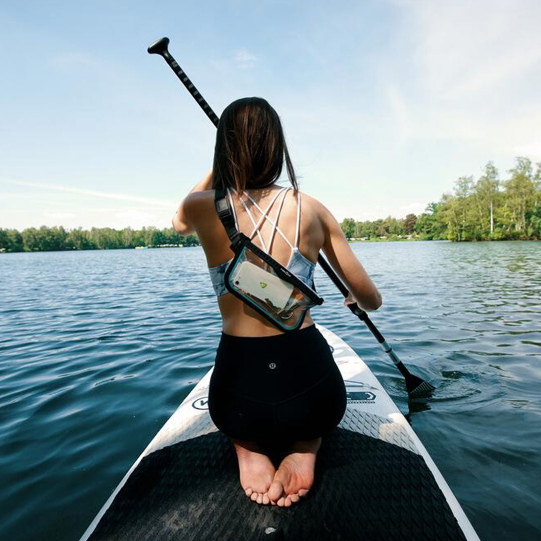 Woman paddleboarding with a waterproof phone pouch in a Fidlock Dry Bag Sling Bag