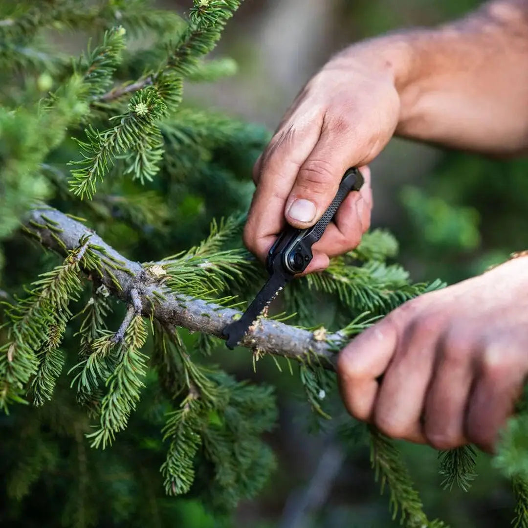 Hands using Gerber Armbar Scout shears to trim an evergreen branch for easy access