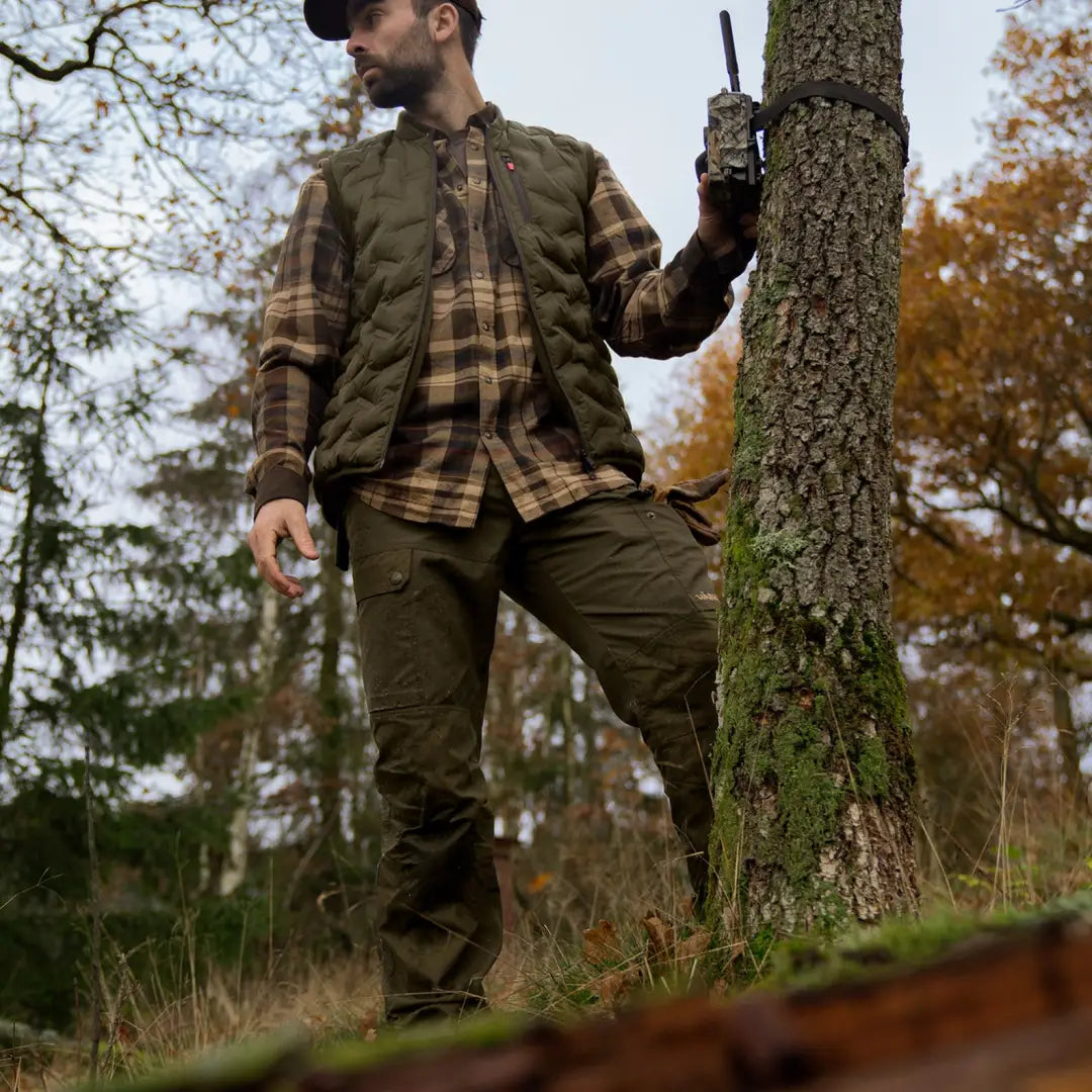 Man in hunting gear with walkie-talkie by tree wearing Harkila Asmund Trousers