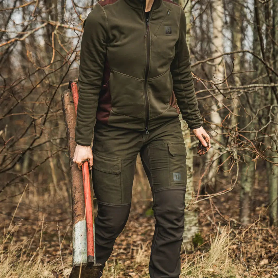 Person in dark green Scandinavian trousers holding an axe in the woods for hunting