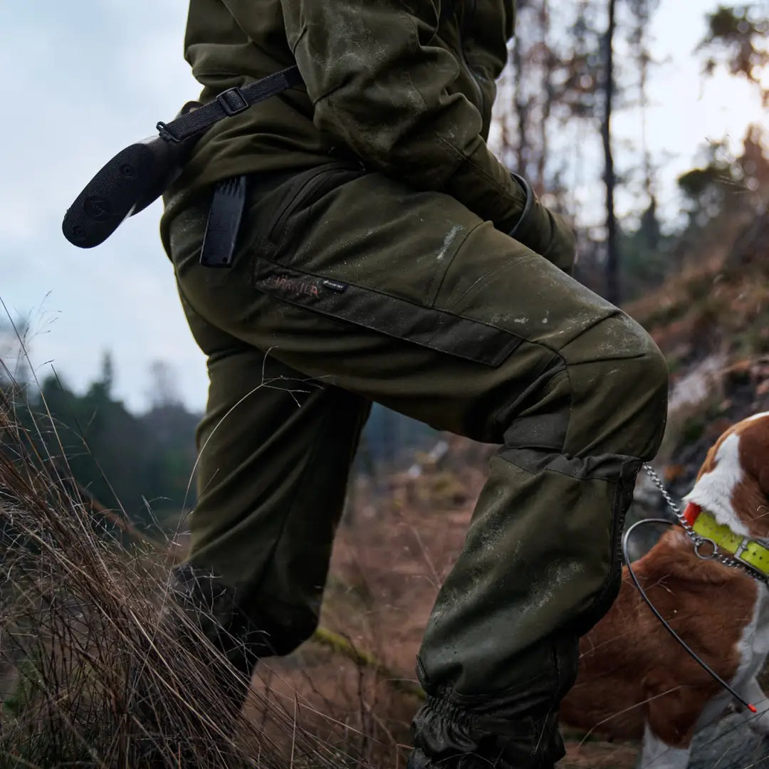 Olive green waterproof Harkila Pro Hunter Move Trousers with thigh pockets on a hiker