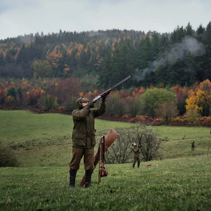 Hunter aiming a shotgun in a field wearing Harkila Pro Hunter Shooting GTX Jacket