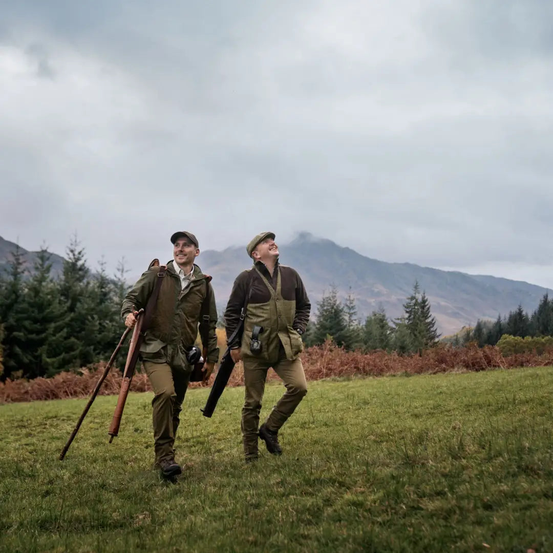 Two hunters with shotguns in a grassy field wearing Harkila Rannoch HWS Shooting Jacket