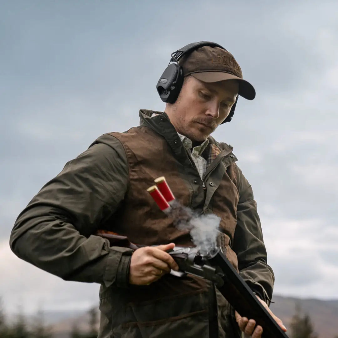 Man in a cap and jacket with a smoking shotgun wearing Harkila Rannoch HWS Shooting Jacket