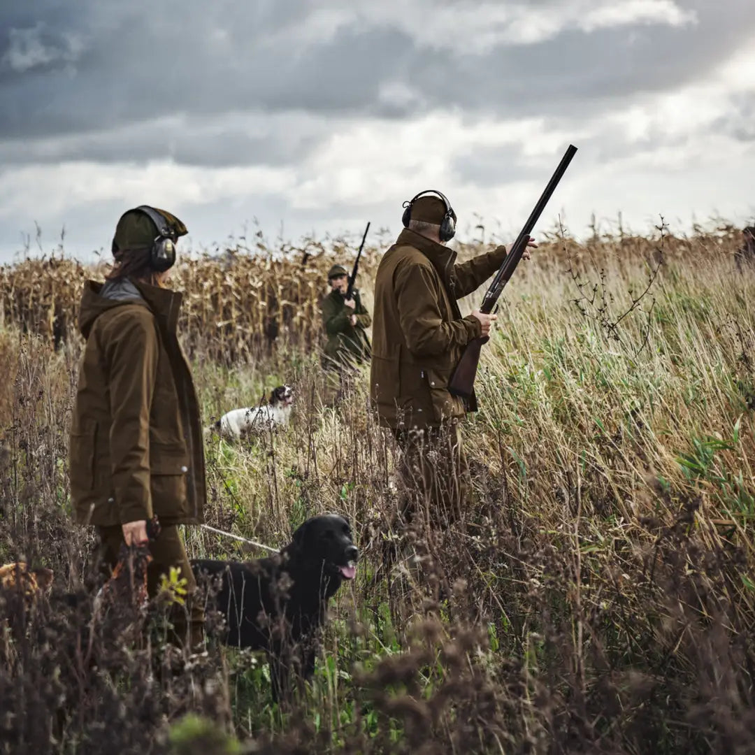 Hunters with shotguns and dogs wear a hardwearing Retrieve Jacket in tall grass