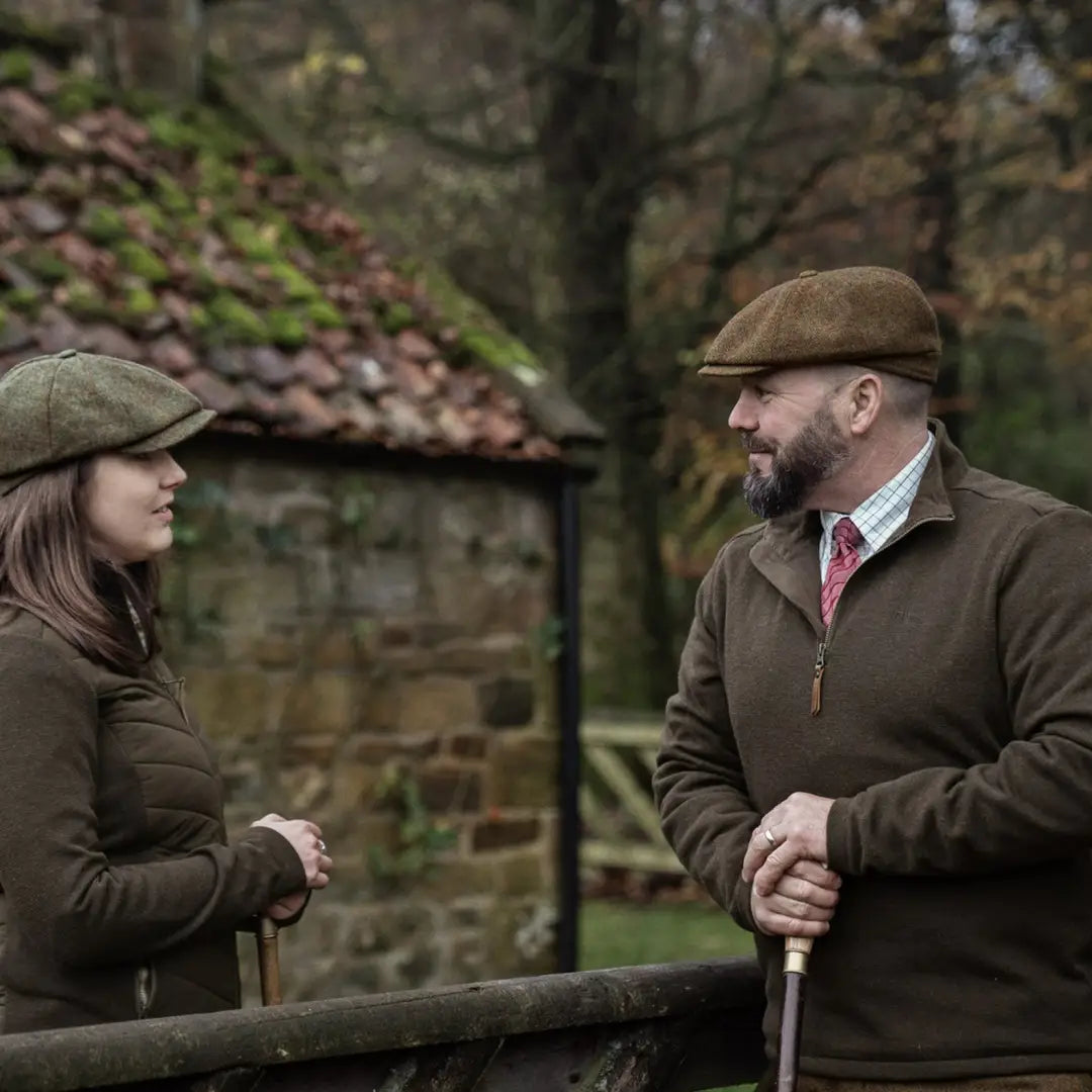 Two folks in country clothing chatting over a fence while wearing a fleece pullover