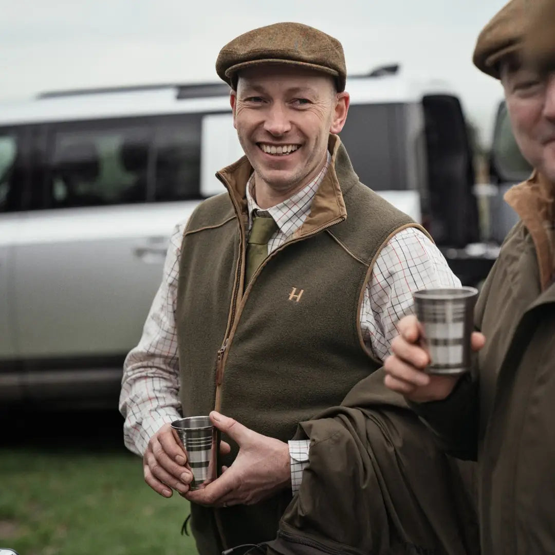 Smiling man in Harkila Sandhem waistcoat enjoying a drink, perfect for country clothing