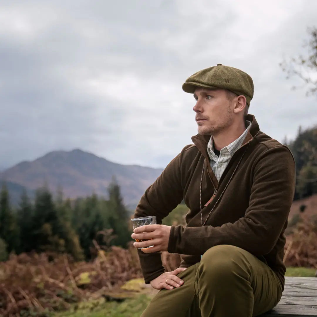 Man in a flat cap and brown jacket enjoying a drink while wearing Harkila Sandhem Pro HSP Pullover