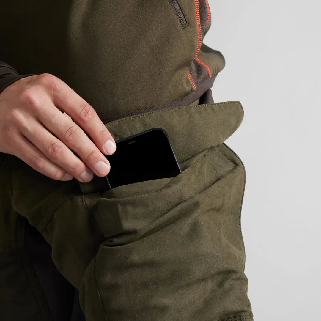 Olive green pocket on Härkila Scandinavian Trousers with a hand inserting a smartphone