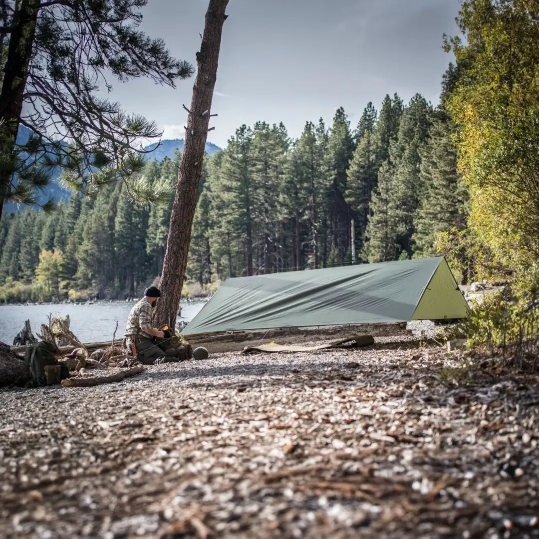 Green Helikon-Tex Supertarp Small camping tent on rocky lakeshore in harsh weather