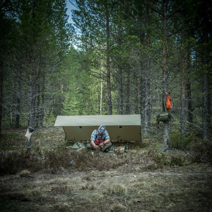 Tent in a forest clearing with person enjoying Helikon-Tex Supertarp Small in harsh weather