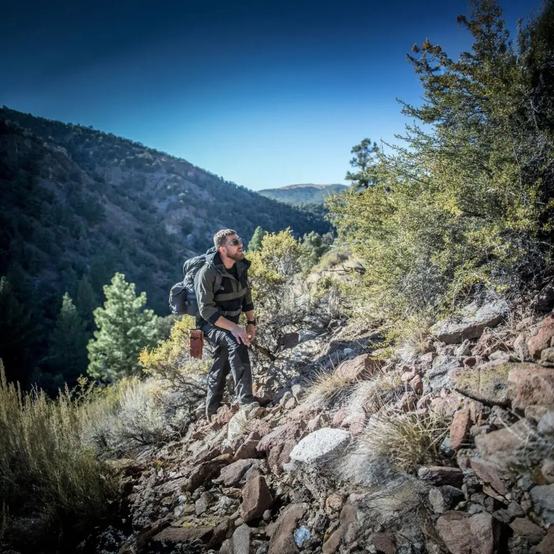 Hiker on rocky trail wearing Helikon-Tex Woodsman Anorak Jacket for outdoor adventure