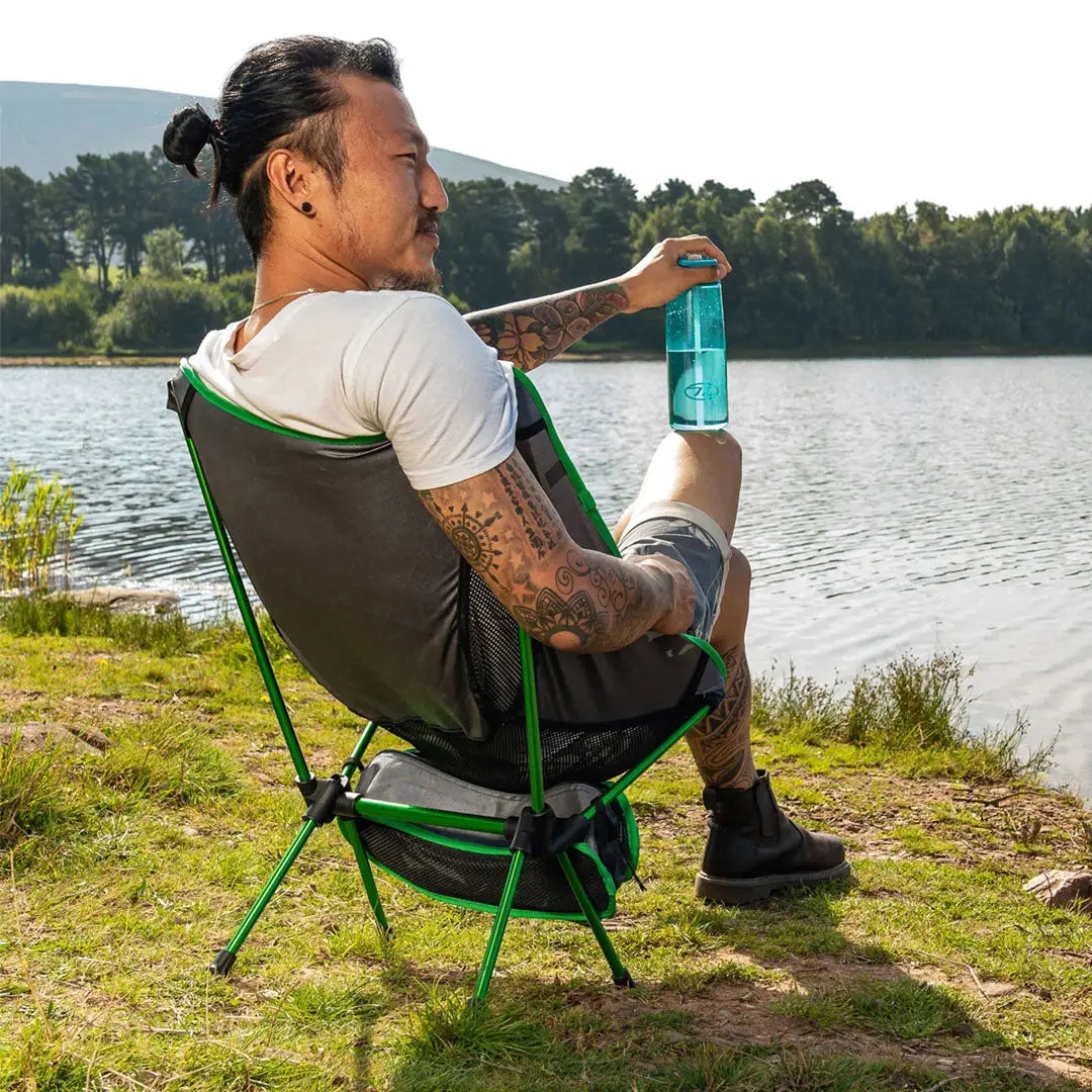 Person enjoying the Highlander Ayr Folding Camping Chair by a serene lake