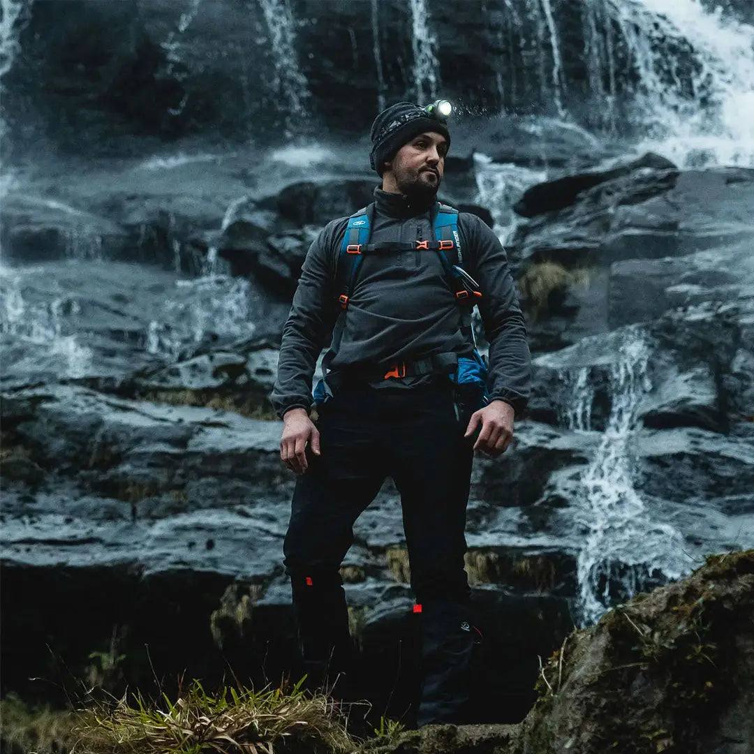 Bearded hiker in outdoor gear with Highlander Polaris Rechargeable Head Torch by waterfall