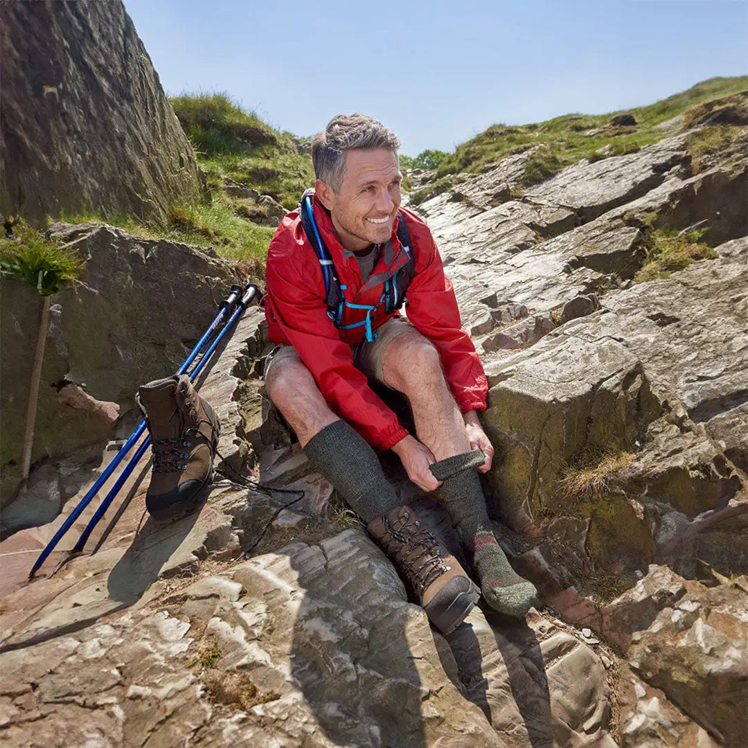 Hiker in a red jacket resting on rocks with ProTrek heavy-duty mountain socks nearby