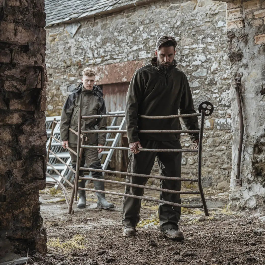 Two men carrying a metal gate in a rustic farm setting with Hoggs of Fife Green King II fleece