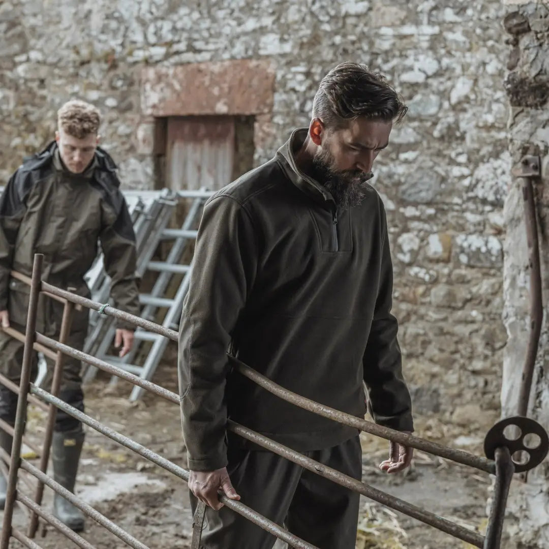 Two men in Hoggs of Fife Green King II fleece carrying ladders in a stone-walled area