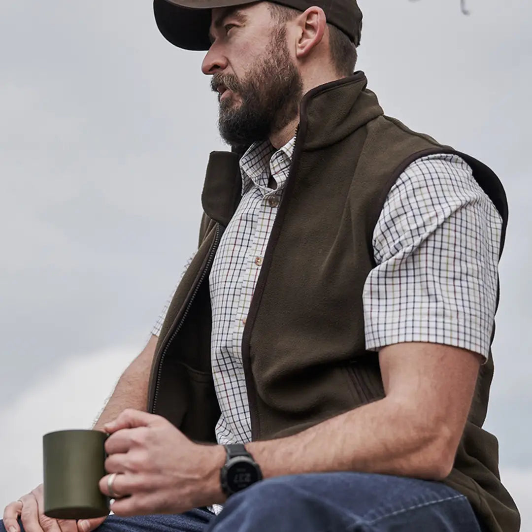 Bearded man in cap and vest holding mug, showcasing Fife Kessock Tattersall Short Sleeve Shirt